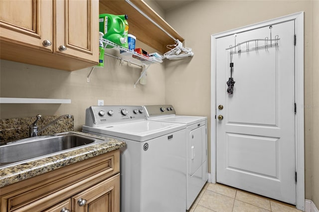 clothes washing area featuring washing machine and dryer, sink, light tile patterned flooring, and cabinets