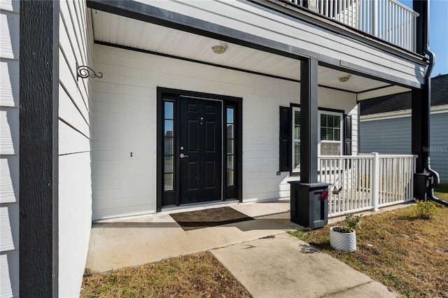 view of exterior entry featuring covered porch and a balcony