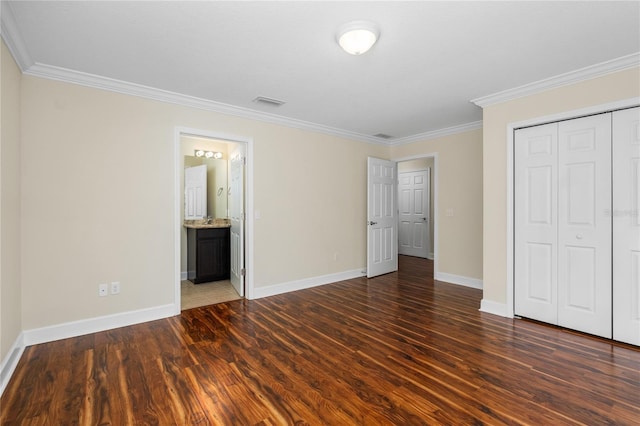 unfurnished bedroom with ensuite bathroom, dark hardwood / wood-style flooring, ornamental molding, and a closet