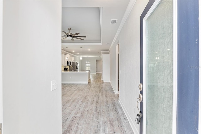 hallway with light wood-type flooring, a tray ceiling, and ornamental molding