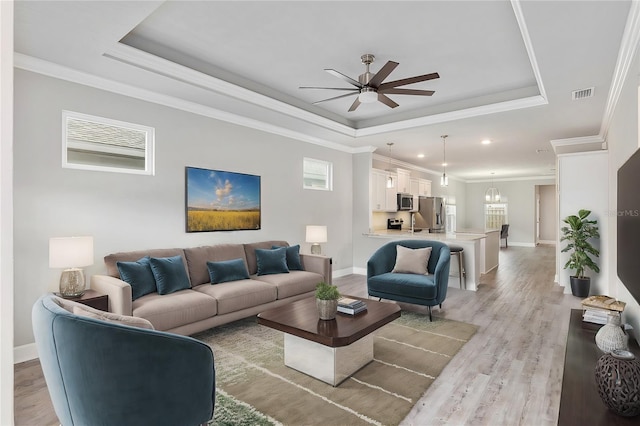 living room with a tray ceiling, ceiling fan, light hardwood / wood-style flooring, and ornamental molding