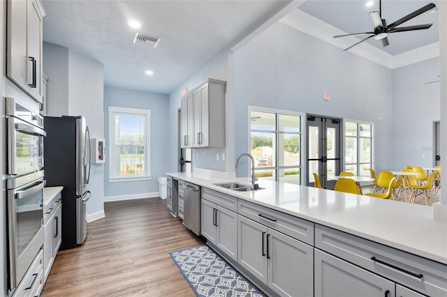 kitchen featuring sink, gray cabinets, light wood-type flooring, ornamental molding, and stainless steel appliances