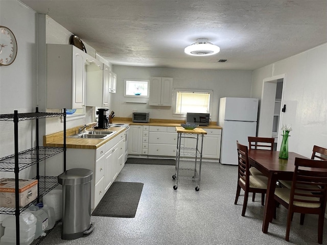 kitchen featuring wooden counters, white cabinets, sink, a textured ceiling, and white fridge