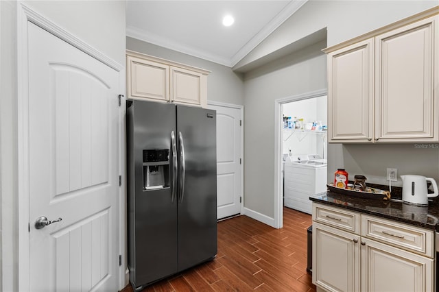 kitchen featuring stainless steel fridge with ice dispenser, cream cabinetry, dark stone countertops, washer and clothes dryer, and vaulted ceiling