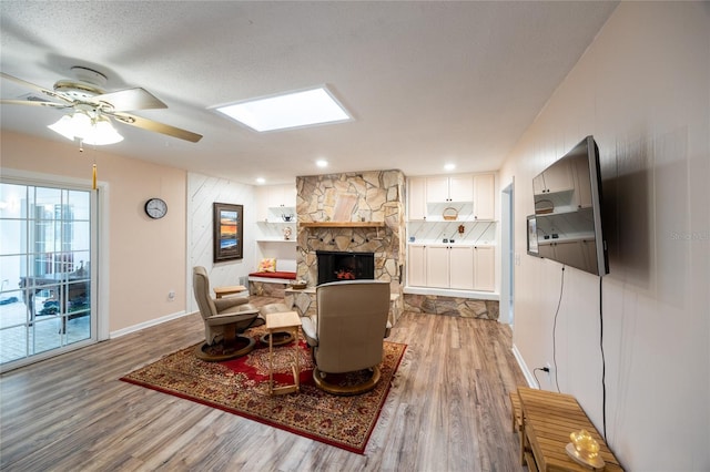 living room featuring a skylight, a textured ceiling, ceiling fan, hardwood / wood-style floors, and a stone fireplace