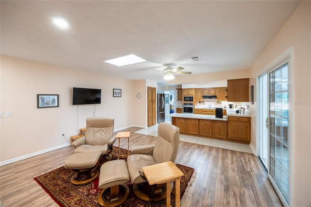 living room with a skylight, ceiling fan, and light hardwood / wood-style floors