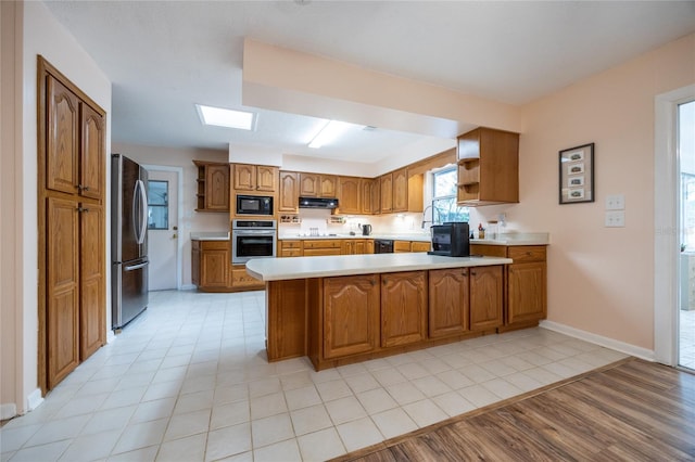 kitchen with light hardwood / wood-style floors, kitchen peninsula, exhaust hood, and appliances with stainless steel finishes