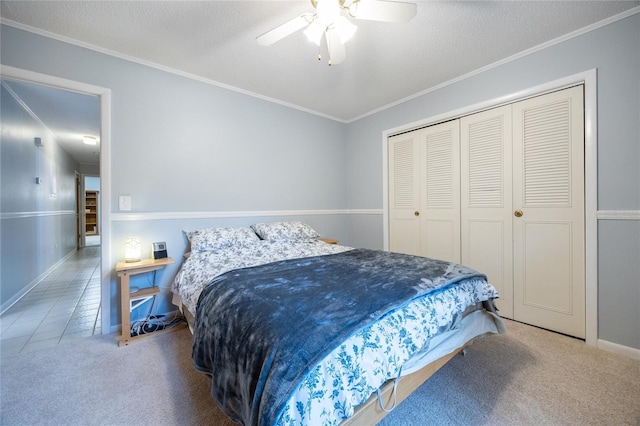 bedroom featuring carpet flooring, a textured ceiling, ceiling fan, crown molding, and a closet