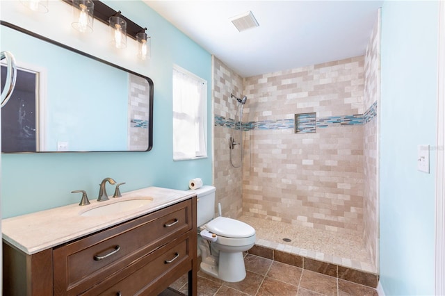 bathroom with tiled shower, vanity, toilet, and tile patterned flooring