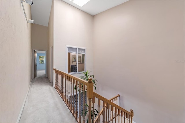 hallway with a skylight, light colored carpet, and a high ceiling