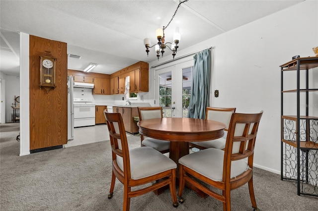 dining room featuring a textured ceiling, light colored carpet, and an inviting chandelier