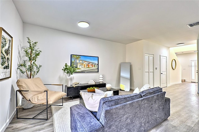 living room with light wood-type flooring, baseboards, and visible vents