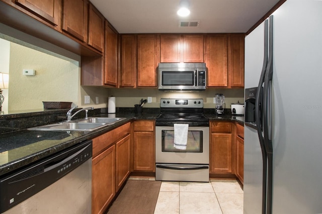 kitchen featuring sink, light tile patterned floors, stainless steel appliances, and dark stone counters