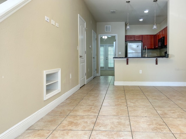 kitchen with a breakfast bar, built in shelves, light tile patterned floors, decorative light fixtures, and stainless steel refrigerator