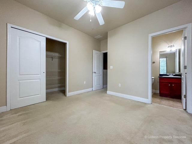 unfurnished bedroom featuring ceiling fan, a closet, light colored carpet, and ensuite bath