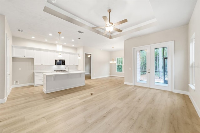 kitchen with white cabinetry, french doors, a raised ceiling, a center island with sink, and ceiling fan with notable chandelier