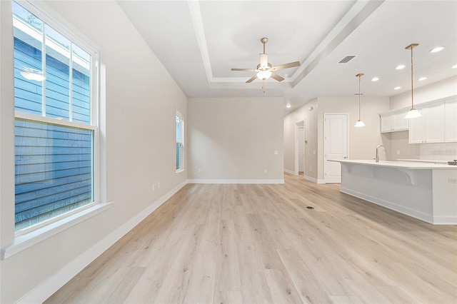 unfurnished living room with light hardwood / wood-style floors, a raised ceiling, ceiling fan, and sink