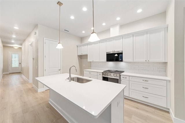 kitchen with high end stove, sink, an island with sink, and decorative light fixtures