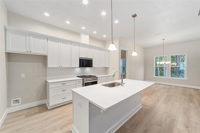 kitchen featuring tasteful backsplash, stainless steel gas range oven, sink, decorative light fixtures, and an island with sink