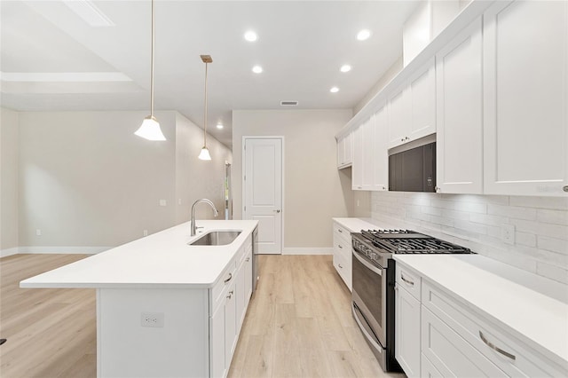 kitchen with white cabinetry, sink, stainless steel gas range, decorative light fixtures, and a kitchen island with sink