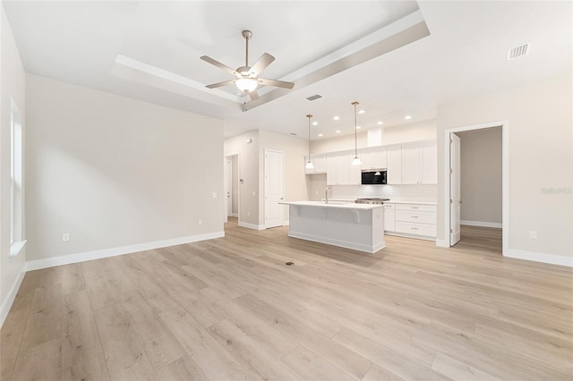 unfurnished living room featuring light hardwood / wood-style floors, a raised ceiling, ceiling fan, and sink