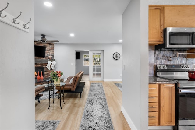 kitchen with decorative backsplash, appliances with stainless steel finishes, ceiling fan, a fireplace, and light hardwood / wood-style floors