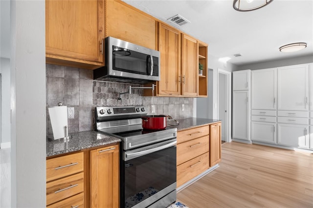 kitchen with appliances with stainless steel finishes, tasteful backsplash, dark stone counters, and light hardwood / wood-style floors