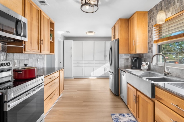 kitchen featuring appliances with stainless steel finishes, tasteful backsplash, sink, light hardwood / wood-style flooring, and dark stone countertops