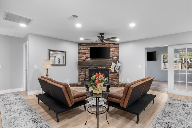 living room featuring ceiling fan, a fireplace, and light hardwood / wood-style flooring