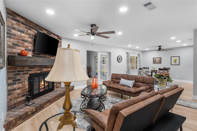 living room featuring a fireplace, light wood-type flooring, and ceiling fan