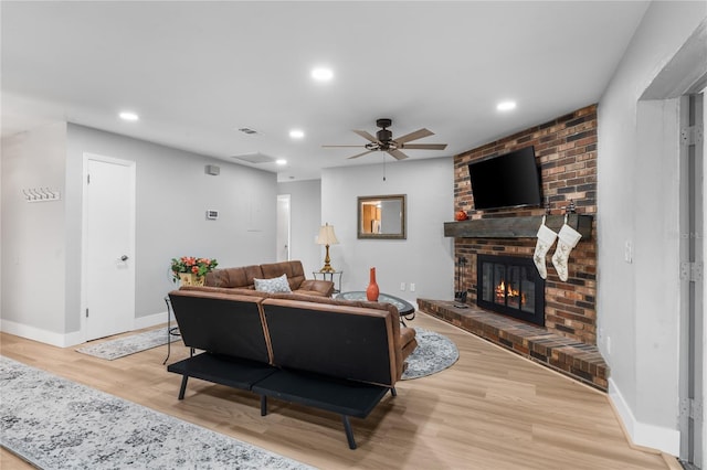 living room featuring a brick fireplace, ceiling fan, and light wood-type flooring