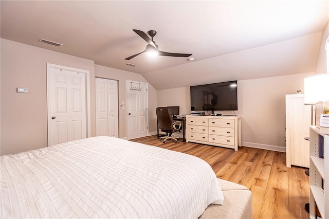 bedroom featuring ceiling fan, vaulted ceiling, two closets, and light hardwood / wood-style flooring