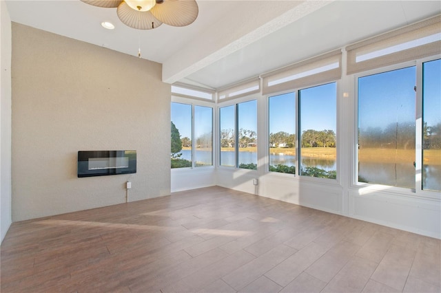 unfurnished sunroom with beam ceiling, heating unit, ceiling fan, and a water view