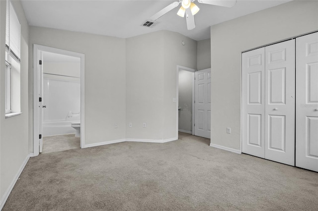 unfurnished bedroom featuring ceiling fan, light colored carpet, ensuite bathroom, and a closet