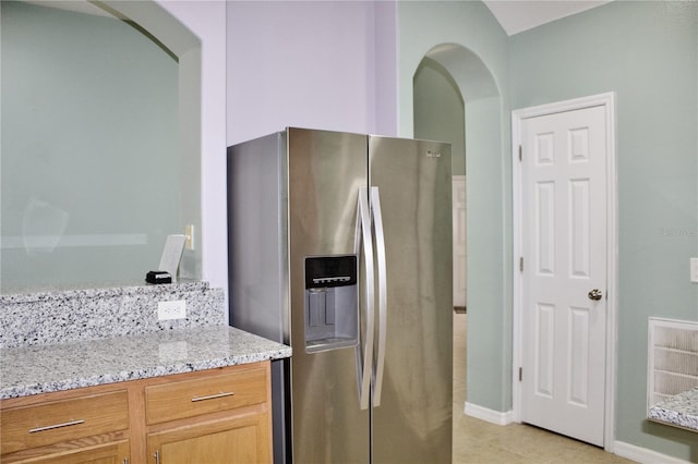 kitchen featuring stainless steel fridge, light tile patterned floors, and light stone counters