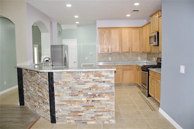 kitchen featuring kitchen peninsula, tasteful backsplash, light stone counters, stainless steel appliances, and light brown cabinets