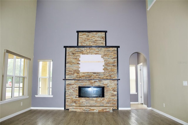 unfurnished living room featuring hardwood / wood-style flooring, a stone fireplace, and a towering ceiling