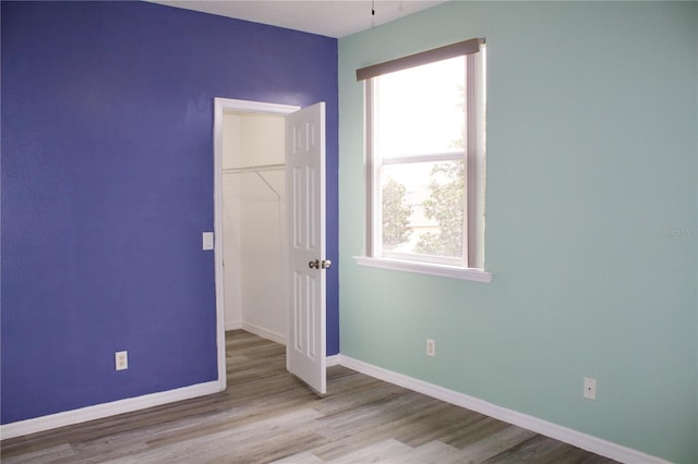 unfurnished bedroom with a spacious closet, light wood-type flooring, and a closet