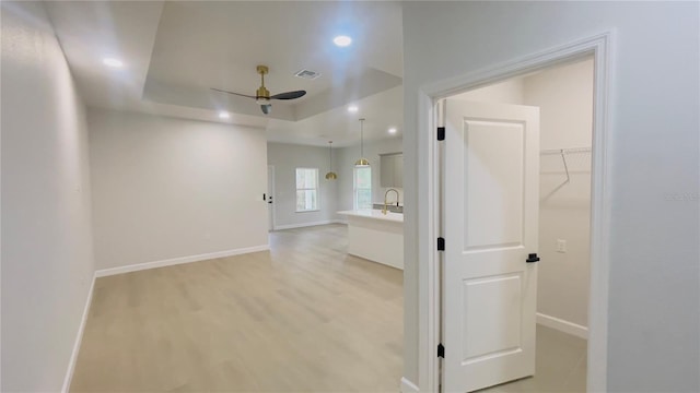 corridor with a tray ceiling, sink, and light hardwood / wood-style floors