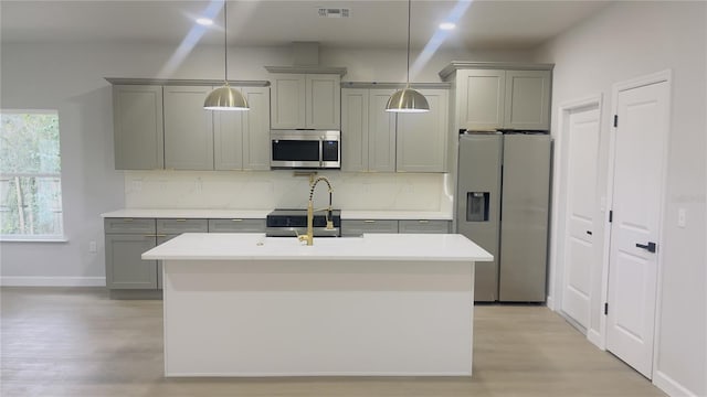 kitchen featuring a center island with sink, decorative backsplash, gray cabinets, decorative light fixtures, and stainless steel appliances