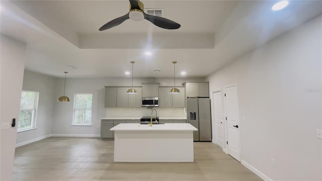 kitchen featuring gray cabinetry, decorative light fixtures, a center island with sink, and stainless steel appliances