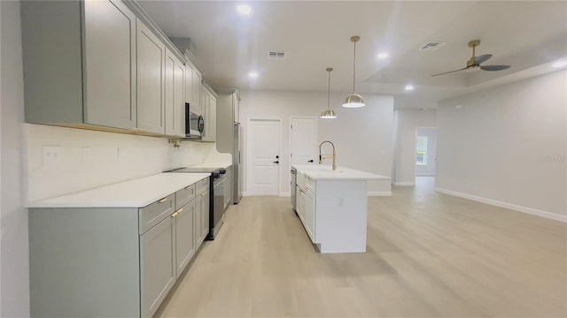 kitchen with gray cabinetry, ceiling fan, decorative light fixtures, a center island with sink, and appliances with stainless steel finishes