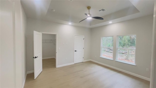 unfurnished bedroom with a raised ceiling, ceiling fan, a spacious closet, light hardwood / wood-style floors, and a closet