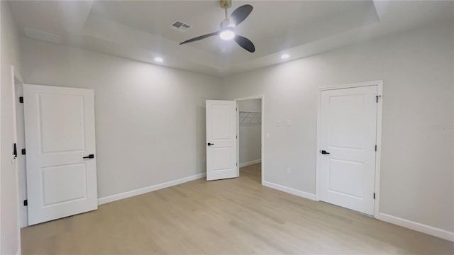 unfurnished bedroom featuring a walk in closet, a raised ceiling, ceiling fan, light hardwood / wood-style flooring, and a closet