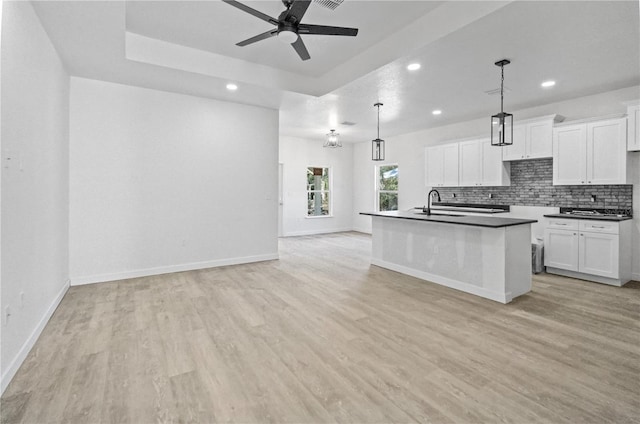 kitchen with decorative light fixtures, sink, white cabinetry, and an island with sink