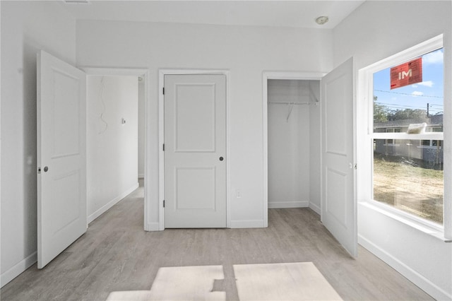 unfurnished bedroom with two closets, light wood-type flooring, and multiple windows