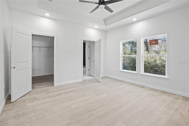 unfurnished bedroom featuring a tray ceiling, ceiling fan, a spacious closet, light hardwood / wood-style flooring, and a closet