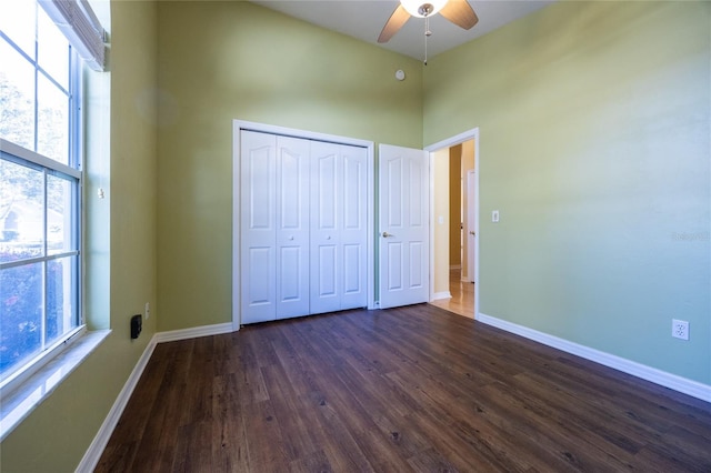 unfurnished bedroom with dark hardwood / wood-style floors, a closet, multiple windows, and ceiling fan