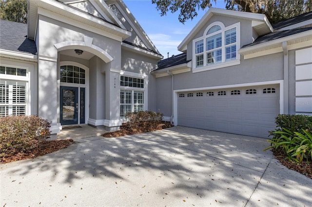 property entrance with concrete driveway, roof with shingles, a garage, and stucco siding