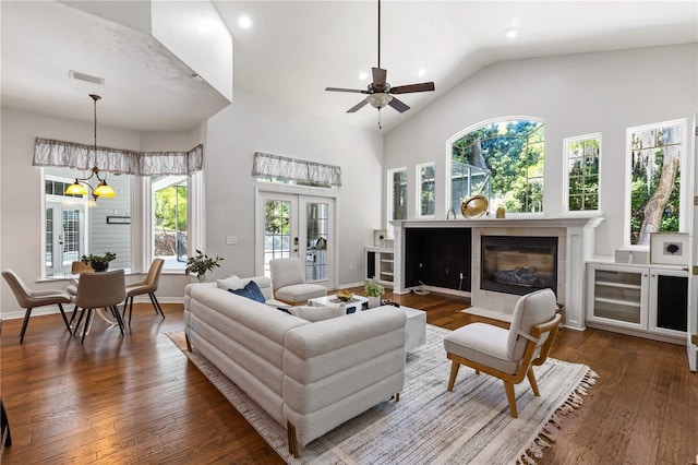 living area with high vaulted ceiling, ceiling fan with notable chandelier, a tile fireplace, dark wood-type flooring, and visible vents